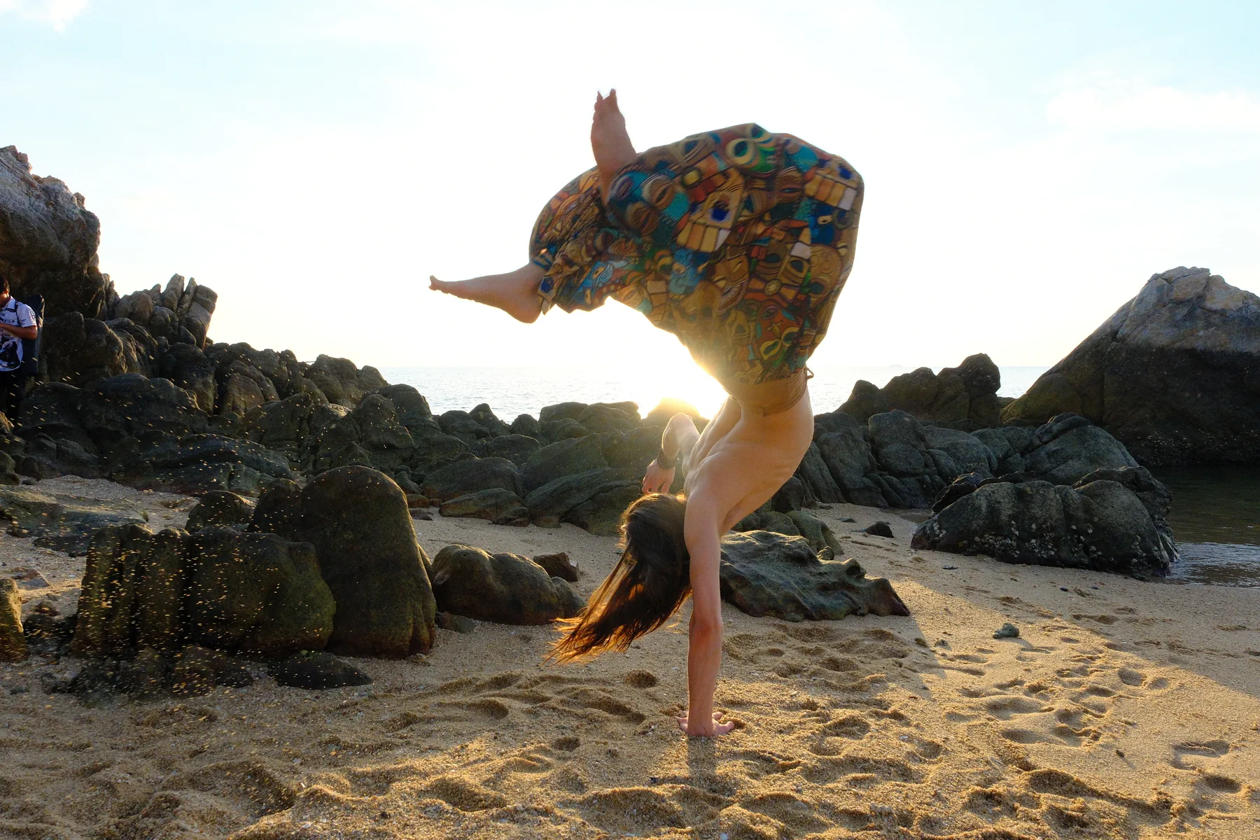 A movement artist balancing on a rocky shoreline